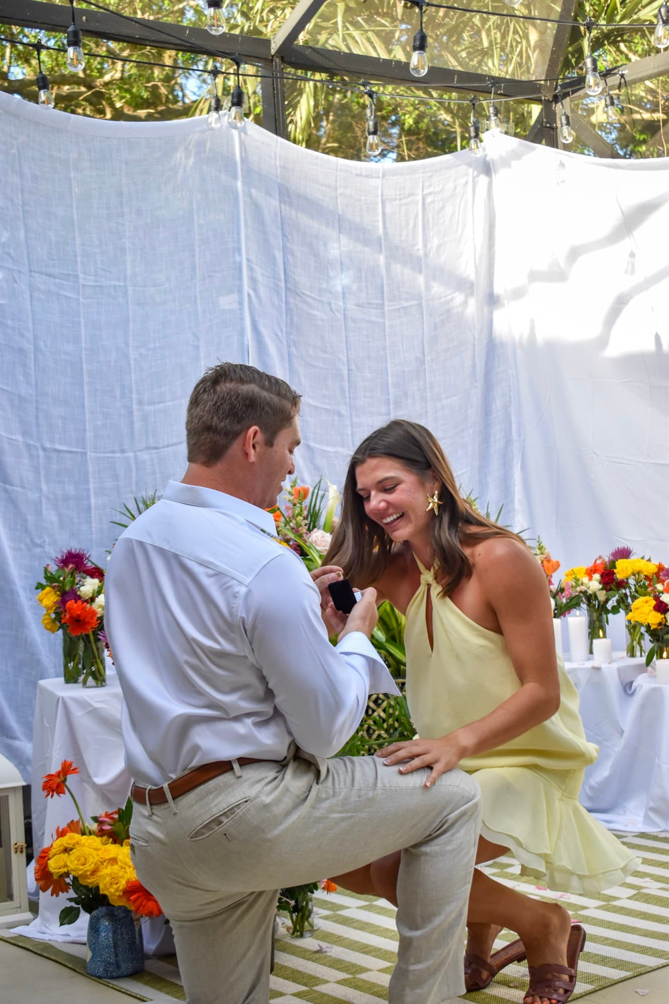 Jon on one knee with the open ring box as Morgan sinks down to his level, laughing.