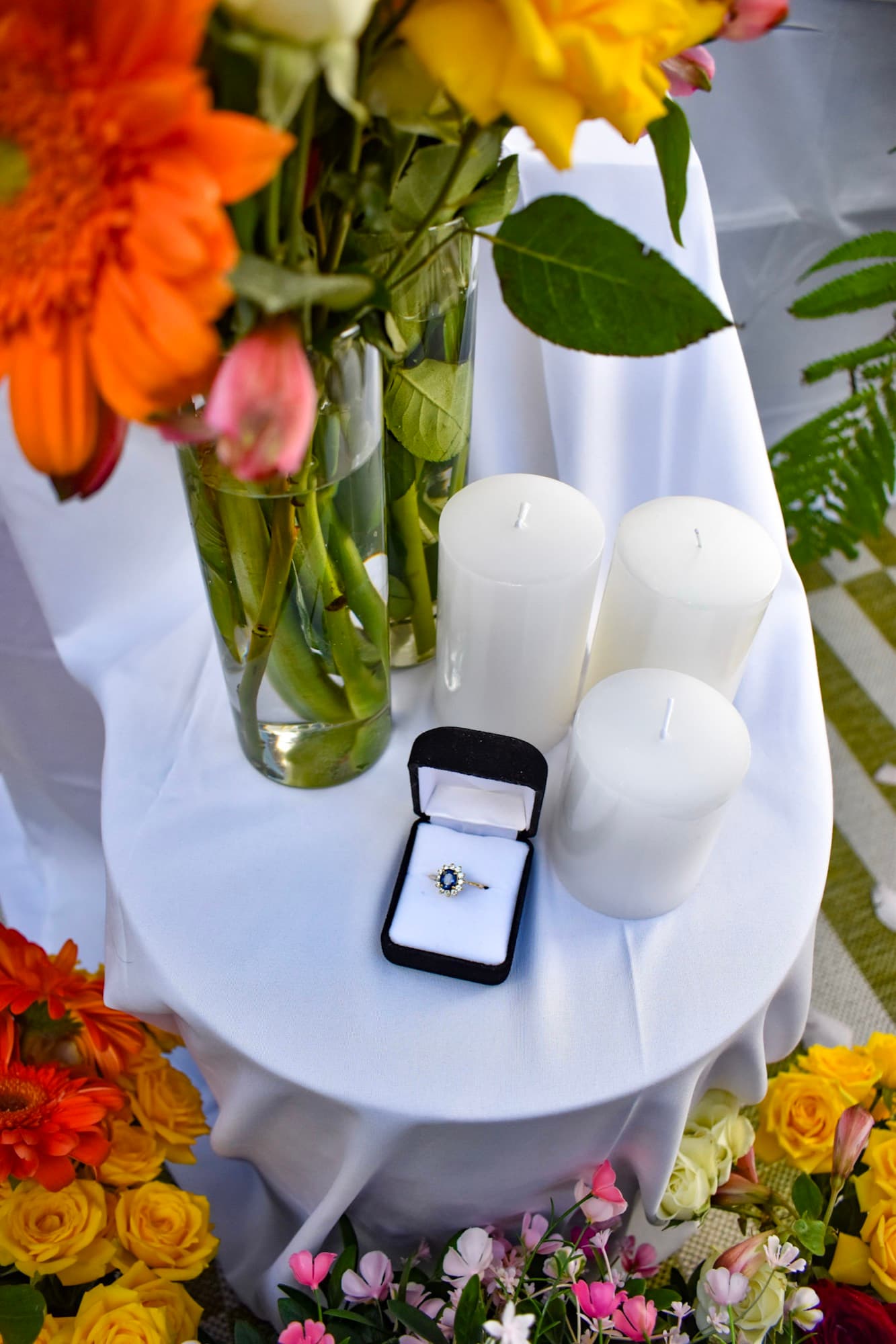 The ring in its box on a linen-covered table, surrounded by pillar candles and bright cut flowers.