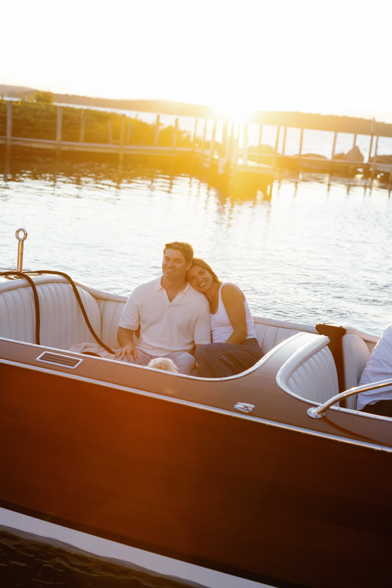 Morgan and Jon tucked into the cockpit of the boat at the dock, sun flaring low over the water behind them.