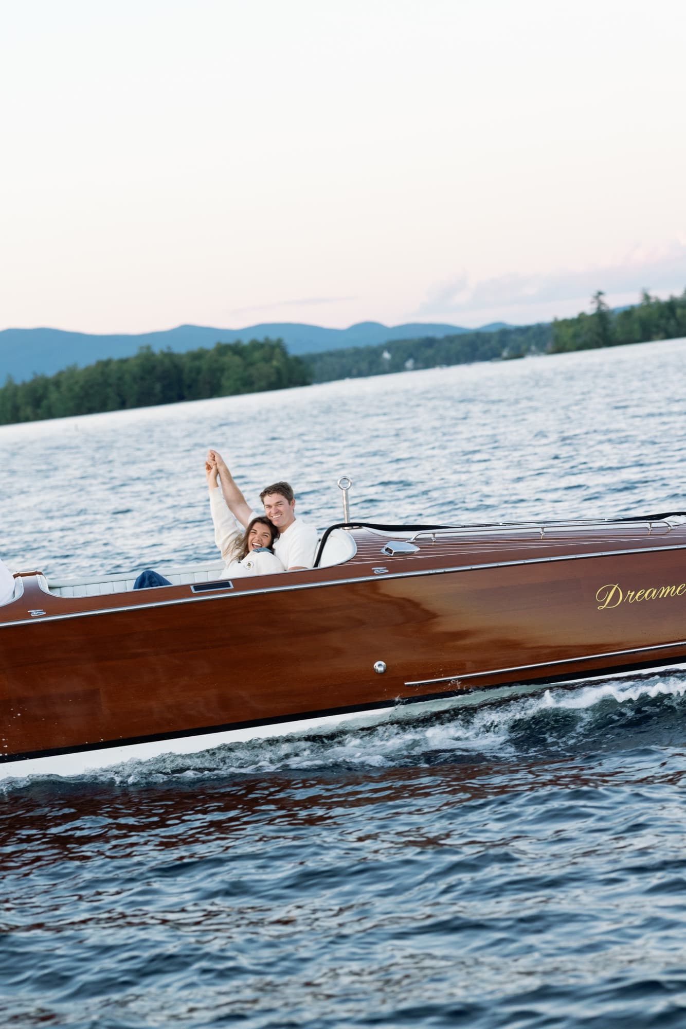 The runabout underway with Morgan and Jon holding their hands up together, wake curling off the hull.